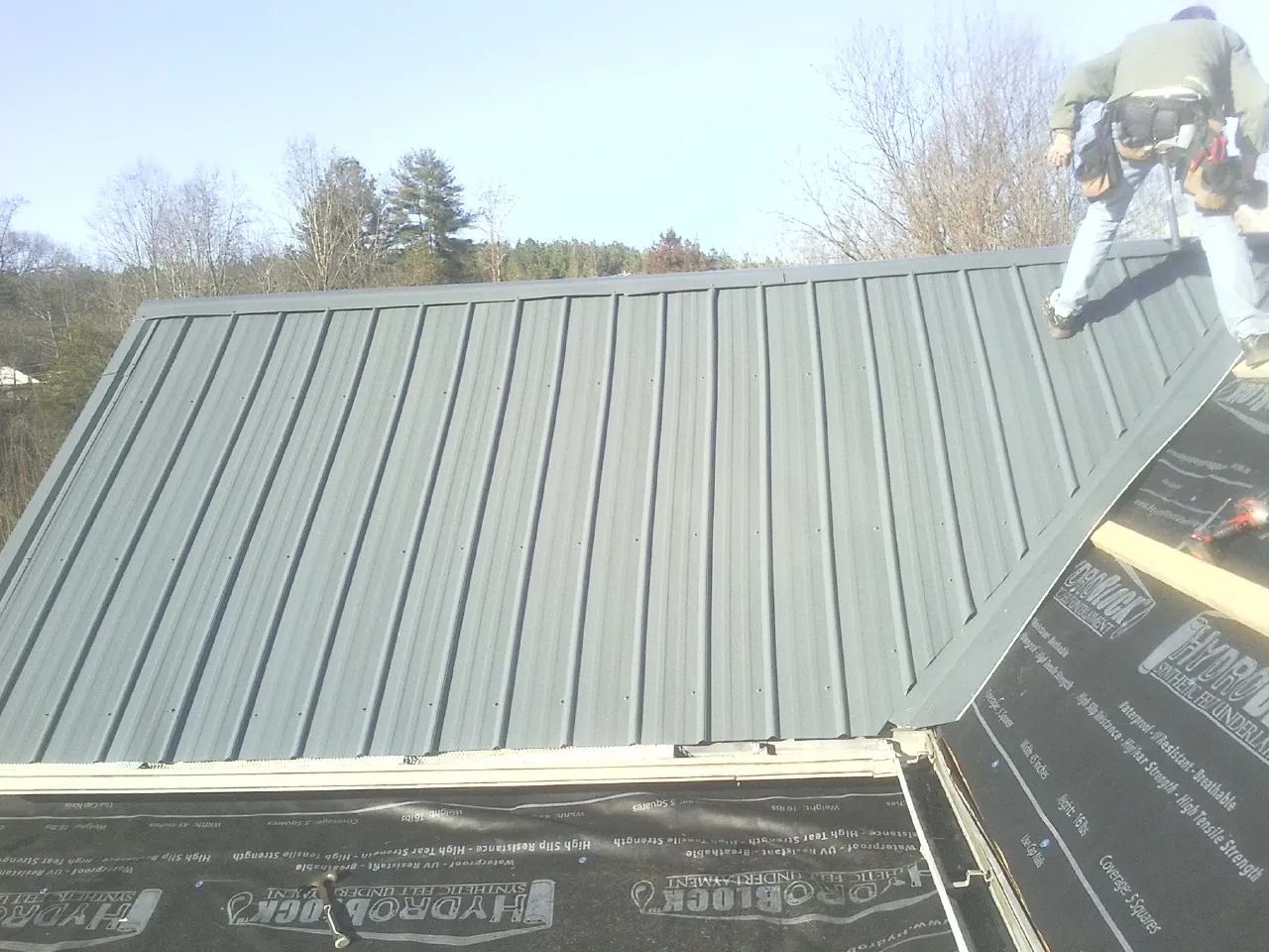 Crew installing dark green standing seam panels over synthetic underlayment in Kalama