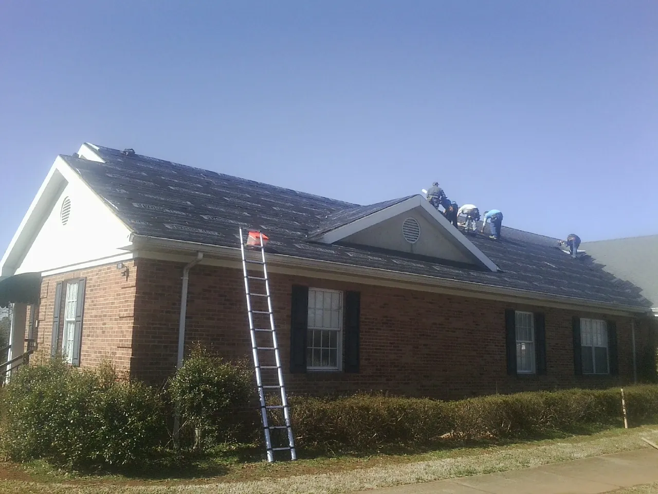Crew tearing shingles off a brick ranch roof with a ladder set — Emergency Roof Repair work by our crew in Kalama