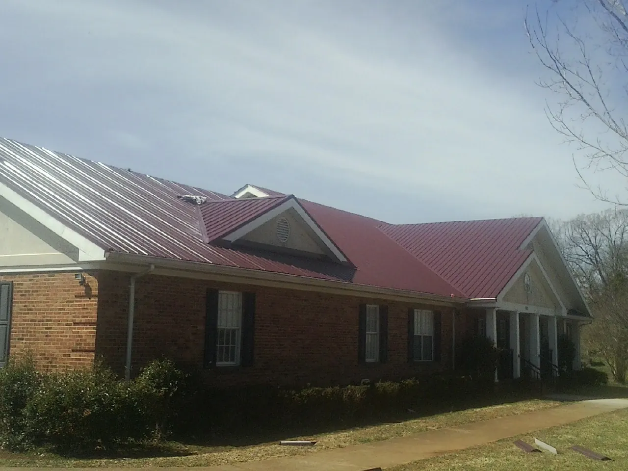 Red metal roof with gabled entries on a long brick building, from a Hail Damage Roof Repair job in Kalama