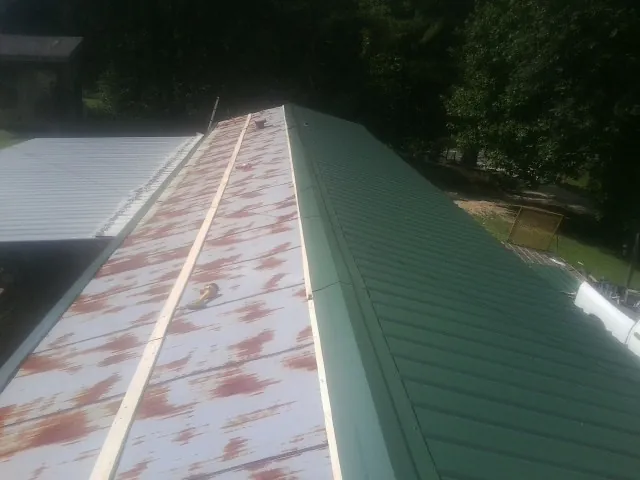 Old rusted panels beside newly installed green metal roofing — Wind Damage Roof Repair by Roofing Brothers in Kalama