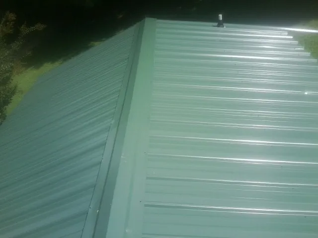 New green metal panels meeting at the ridge of a roof — Flat Roof Repair work by our crew in Kalama