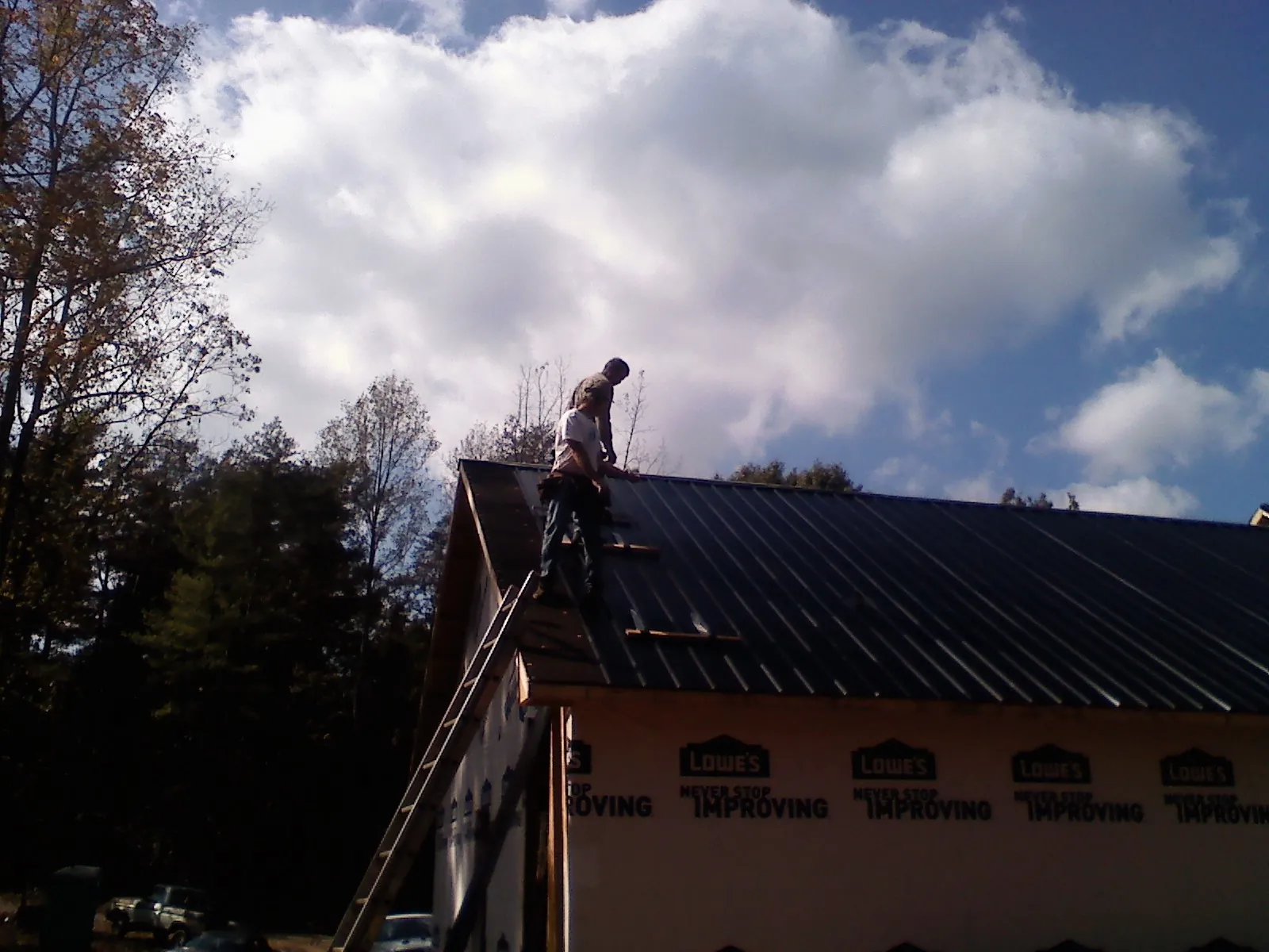 Roofer fastening dark metal panels high against a cloudy sky, from a Roof Inspection job in Kalama