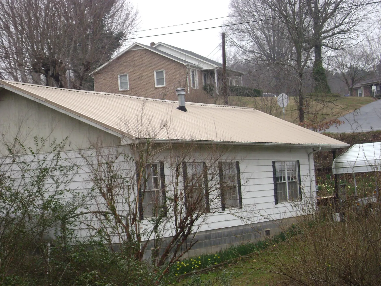 Tan metal roof on a white sided house set into a hillside — Commercial Roofing by Roofing Brothers in Kalama